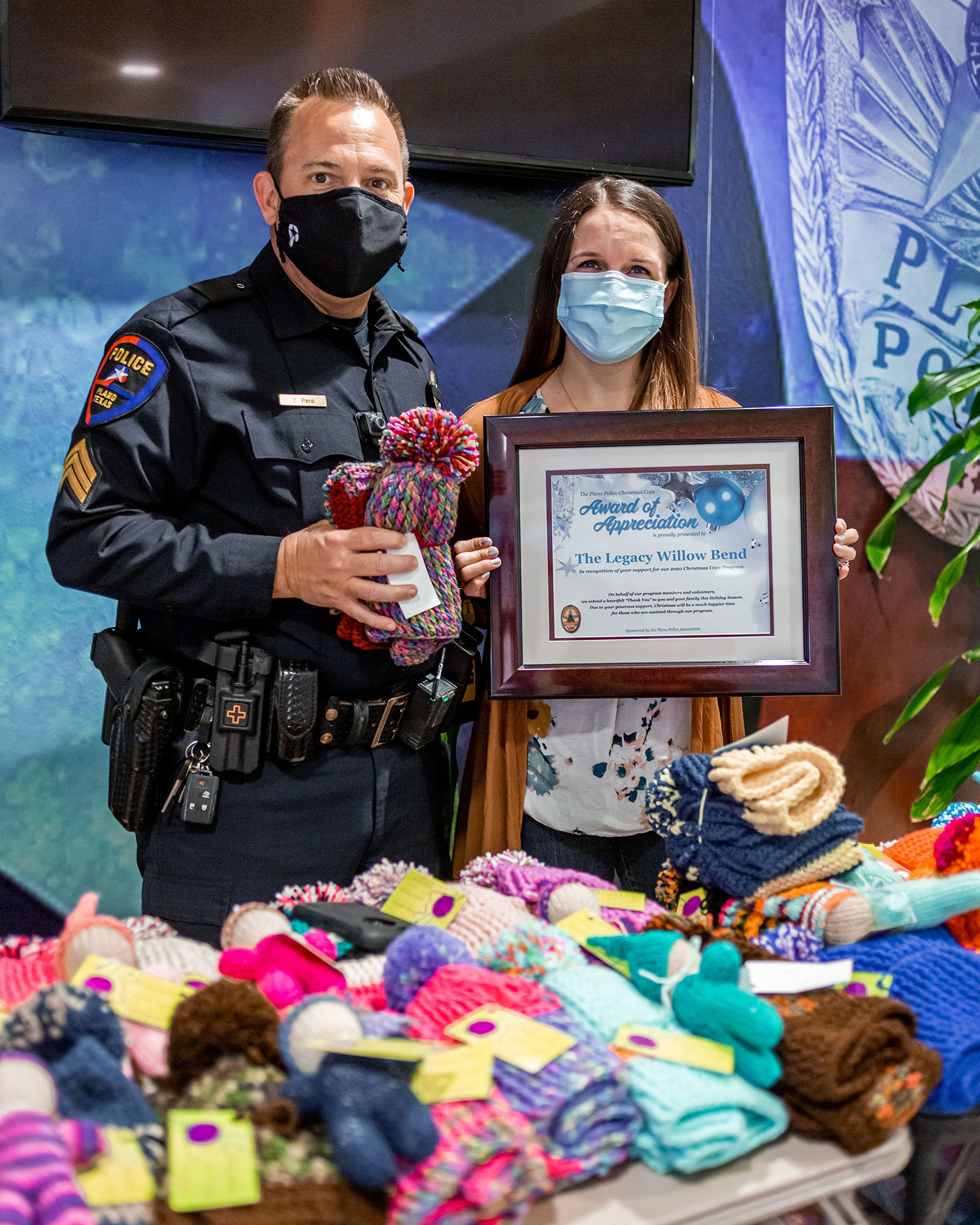 Rivae Campo, volunteer manager at The Legacy Senior Communities, presents hand-knitted items to Plano Police Officer Courtney Pero