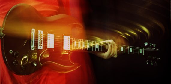 Guitarist lets chord ring out, with intentional motion blur. Cross-processed.