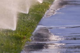 Sprinklers water the grass in the early morning and excess water runs off into the sidewalk