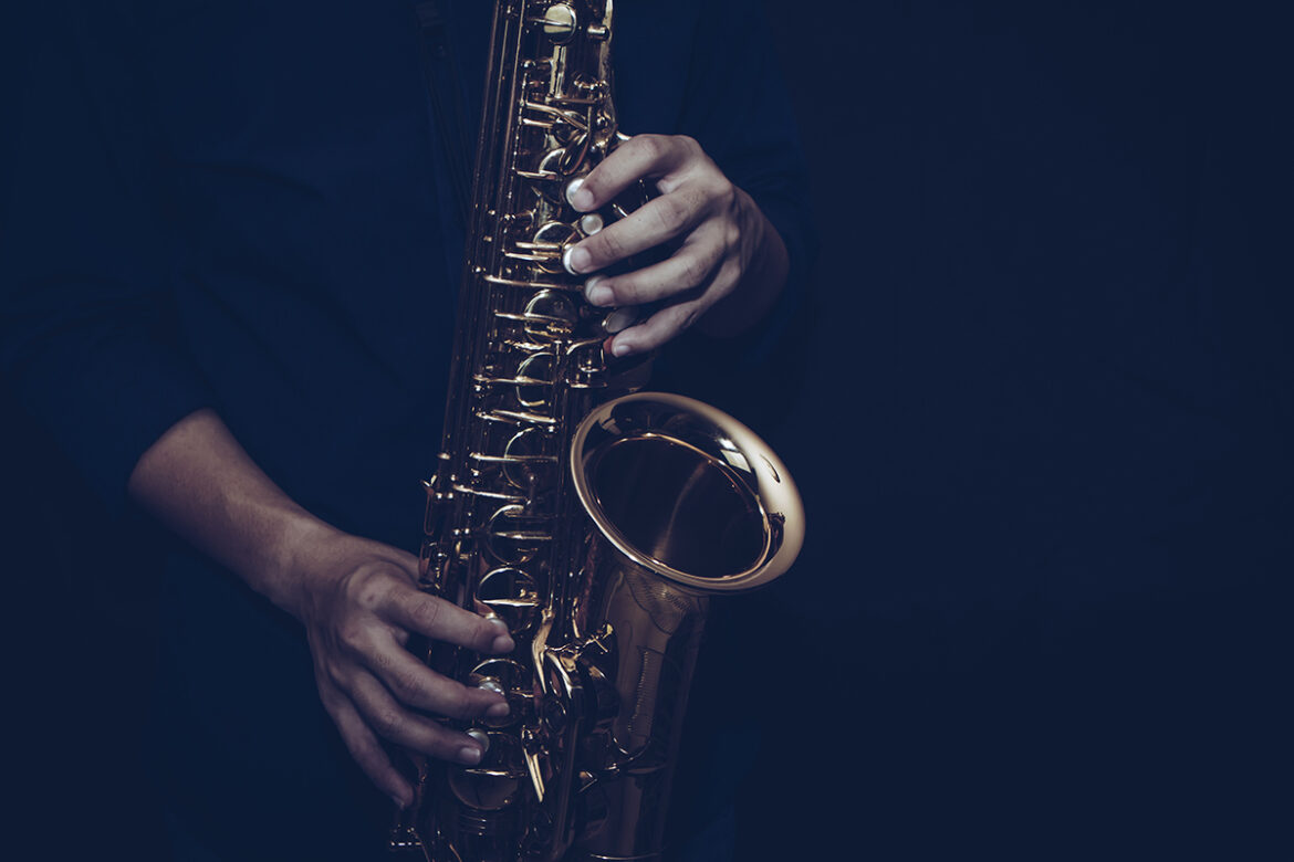 Saxaphone. Getty Image. Close up of a young musician man hands hold and playing saxophone on black background with copy space. Can be used for music poster background