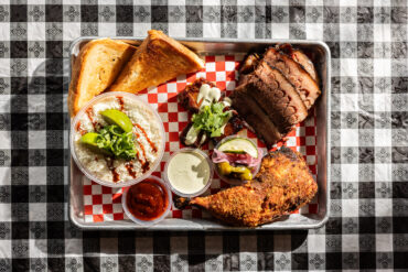 A Burnt BBQ plate containing smoked and fried BBQ citrus chicken, Mexican street corn elote, 14-hour pecan-smoked Black Angus brisket and toast. Photography by Kathy Tran